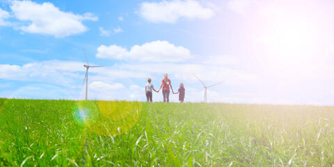 Das Symbolbild soll Akzeptanz von erneuerbaren Energien darstellen und zeigt eine Familie auf einer Wiese und Windräder im Hintergrund (Bildquelle: M.studio - stock.adobe.com)